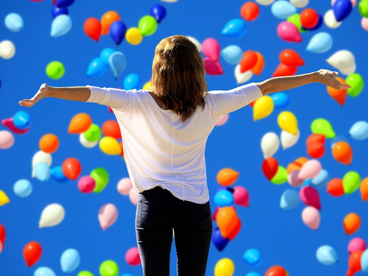 Mujer de espaldas con los brazos extendidos, fondo de globos